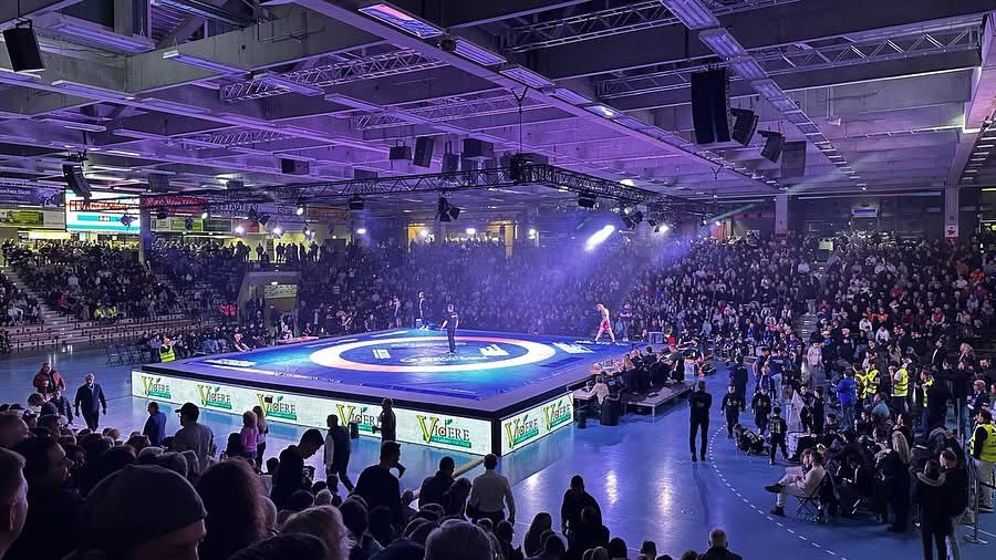 Volle Ringer-Wettkampfarena mit beleuchteter Matte und Publikum.